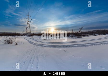 Abendliche Winterlandschaft mit Stromübertragungstürmen und Spuren eines Autos in Südjakutien, Russland Stockfoto