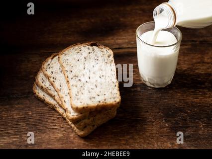 Brotstücke mit Samen und Milch werden in ein Glas gegossen. Dunkler Holzhintergrund. Frühstück am Morgen. Gesunde Ernährung. Stockfoto