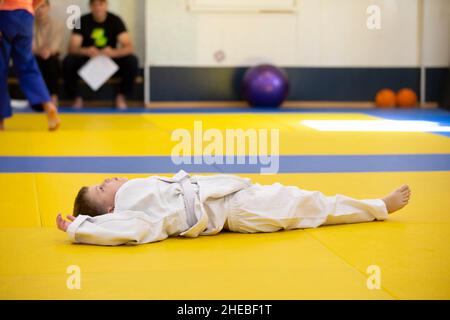 Weißrussland, die Stadt Gomil, 23. Juni 2021. Judo Club. Ein Kind in einem Kimono liegt im Fitnessstudio auf Matten. Stockfoto