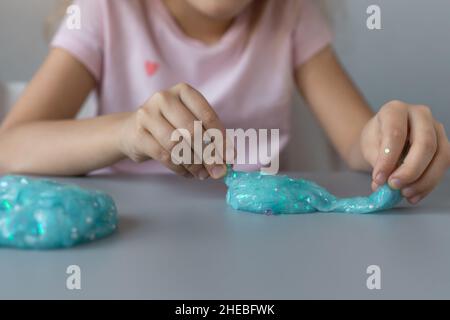 Kind spielt zu Hause am grauen Schreibtisch mit blauem Schleim Stockfoto