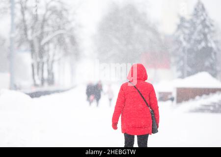 Weißrussland, Stadt Gomil, 11. Februar 2021. Stadtstraße in einem Schneesturm. Eine Frau geht während eines Schneefalls die Straße entlang. Mädchen an einem Wintertag. Stockfoto