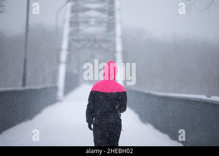 Eine Frau geht während eines Schneefalls die Straße entlang. Mädchen an einem Wintertag. Stockfoto