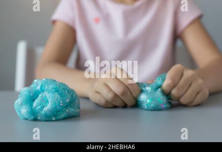 Blauer Glitzerschleim auf grauem Schreibtisch und spielenden Kind Stockfoto