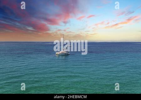 Yacht, die auf dem Mittelmeer Griechenlands driftet und das Boot versteckt, wobei die schaumige Spur unter blauem wolkenlosem Himmel am Horizont zurückbleibt Stockfoto