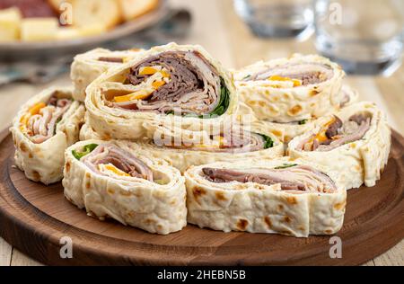 Tortilla-Wraps mit Roastbeef, pute, Käse und Salat auf einer Holzplatte gestapelt Stockfoto