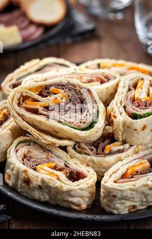 Tortilla-Wraps mit Roastbeef, pute, Käse und Salat auf einem schwarzen Teller Stockfoto