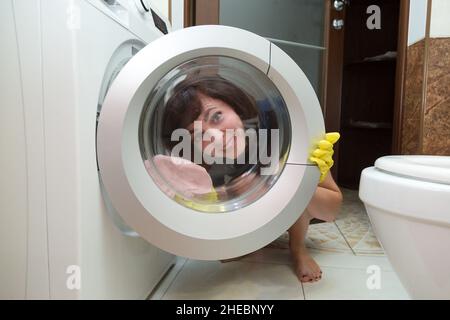 Eine lächelnde Frau mit gelben Gummihandschuhen wäscht Glas in einer Waschmaschine. Stockfoto