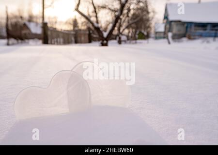 Zwei Herzen - ein Symbol der Liebe, aus Eis, in einer Schneeverwehung, in einem Dorfhof. Valentinstag. Romantisches Konzept. Speicherplatz kopieren. Stockfoto