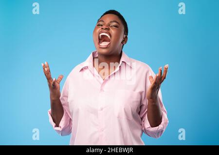 Emotional Übergewichtige Afroamerikanische Frau, Die Über Blauem Hintergrund Steht Und Schreit Stockfoto