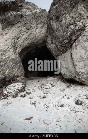 Dunkler Höhleneingang im Winter, schneebedeckter Höhleneingang auf dem Vorderansicht-Foto von der Hügeloberseite Stockfoto