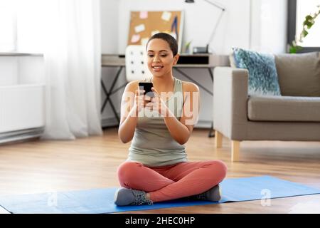 Frau mit Smartphone sitzt zu Hause auf der Trainingsmatte Stockfoto