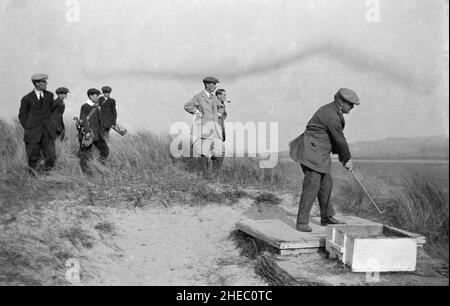 Um 1910, historisch, Golfer auf einem Links-Golfplatz, mit jungen Caddys, einem männlichen Golfer in der Golfkleidung des Tages, der eine kleine hölzerne Plattform abschlug, England, Großbritannien. Stockfoto