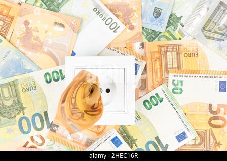 Steigende Stromkosten, teures Energiekonzept. Weiße Steckdose mit Euro-Banknoten Hintergrund Stockfoto