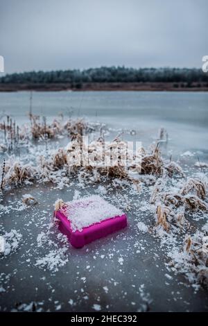 Plastikmüll im gefrorenen Wasser, rosa Stück Plastik mit Schnee bedeckt teilweise in Eis gefroren, Müll im See, Umweltverschmutzung, wilde Mülldeponie Stockfoto