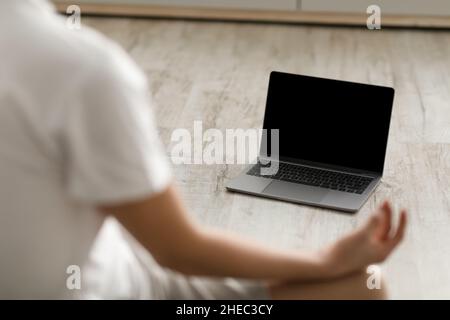Junger Mann, der mit pc in Lotusposition auf einer Matte sitzt Stockfoto