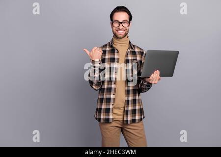 Portrait von attraktiven trendy fröhlich qualifizierten Kerl mit Laptop zeigt Kopierer Raum Lösung isoliert über grauen Hintergrund Stockfoto