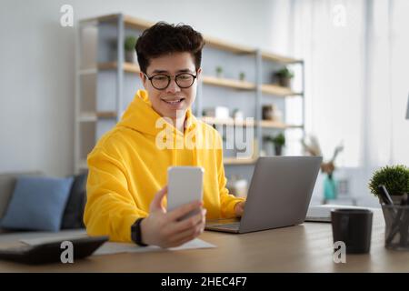 Asiatischer Mann in Brille sitzt am Schreibtisch mit Handy Stockfoto