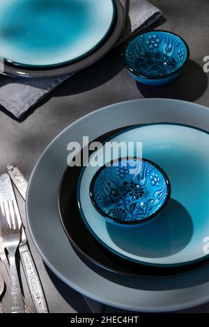 Geschirr, verschiedene Teller in graublauen Farben auf dunklem Tisch mit geometrischen Formen Schatten Stockfoto