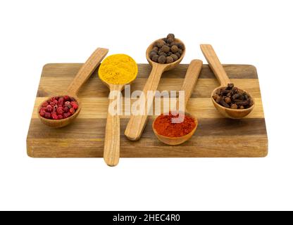 Weißer Hintergrund, isoliert, fünf Löffel mit Gewürzen liegen auf Holzschneidebrett Stockfoto