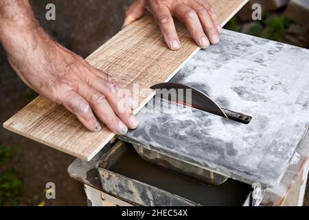 Ein Mann schneidet eine Keramikfliesen mit einem Fliesenschneider mit Wasserkühlung. Nahaufnahme, selektiver Fokus Stockfoto