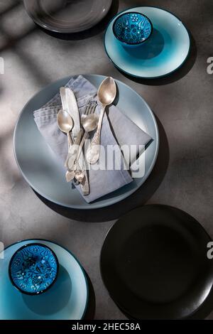 Geschirr, verschiedene Teller in graublauen Farben auf dunklem Tisch mit geometrischen Formen Schatten Stockfoto