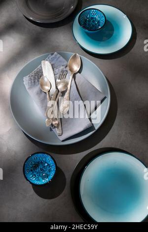 Geschirr, verschiedene Teller in graublauen Farben auf dunklem Tisch mit geometrischen Formen Schatten Stockfoto