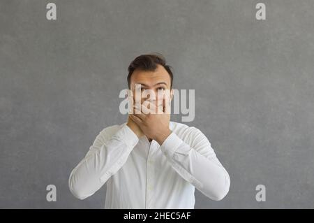 Überrascht und schockiert schließt der junge kaukasische Mann ängstlich seinen Mund mit beiden Händen. Stockfoto