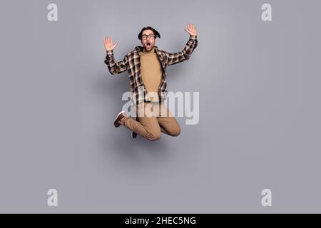 Foto von schockiert funky Kerl gekleidet kariert Hemd Gläser springen hoch isoliert grauen Hintergrund Stockfoto