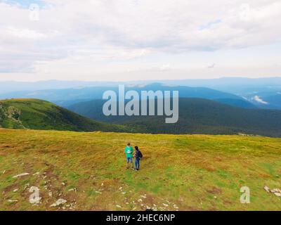 Luftaufnahme des Great Green Ridge. Guy und Girl stehen auf einem großen Hügel vor dem Hintergrund einer riesigen Berglandschaft Stockfoto