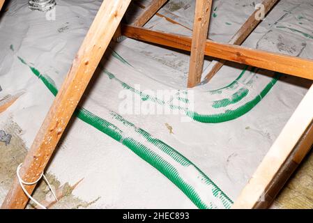 Rohrisolierung mit expandiertem Perlit in der häuslichen Lüftung mit Energierückgewinnung, ein sichtbares System aus grünen Rohren, das sich über die Dachbinder verteilt. Stockfoto