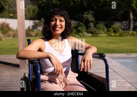 Porträt einer behinderten afroamerikanischen Frau, die auf einem Rollstuhl sitzt und im Garten lächelt Stockfoto