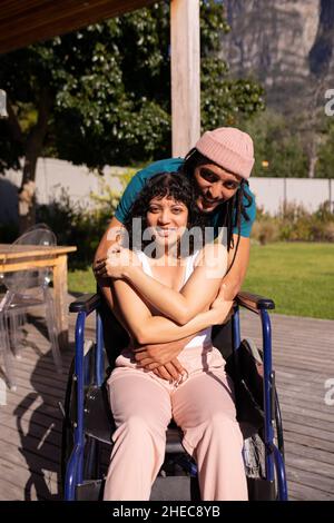 Porträt eines afroamerikanischen Mannes, der seine behinderte Frau im Freien im Rollstuhl umarmt Stockfoto