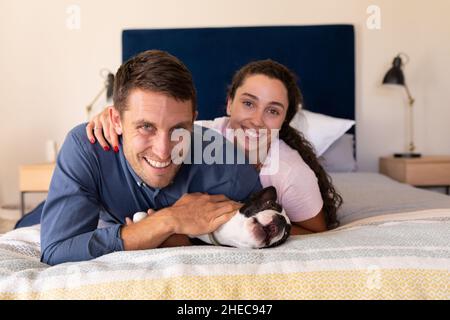 Porträt eines kaukasischen Paares mit lächelndem Hund, der zu Hause auf dem Bett liegt Stockfoto