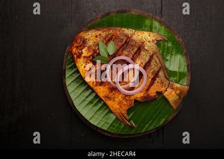 Fischbraten, angeordnet auf einer runden Holzbasis, die mit Bananenblättern ausgekleidet ist Stockfoto