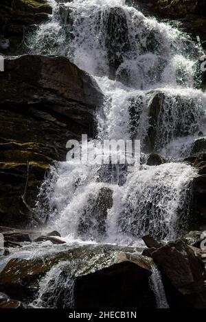 Das Wasser fließt durch einen kleinen Gebirgsbach und fließt über Basaltsteinfelsen. Ein kleiner Wasserfall fließt durch das Moos Stockfoto