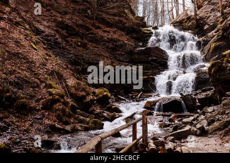 Das Wasser fließt durch einen kleinen Gebirgsbach und fließt über Basaltsteinfelsen. Ein kleiner Wasserfall fließt durch das Moos Stockfoto