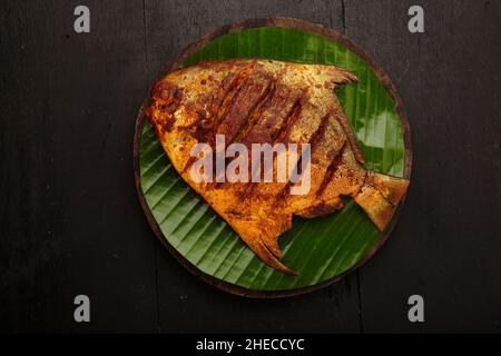 Fischbraten, angeordnet auf einer runden Holzbasis, die mit Bananenblättern ausgekleidet ist Stockfoto