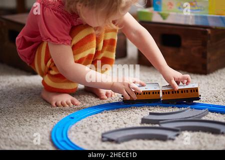 Mädchen spielt mit einem Zug. Pädagogisches Spielzeug für Kinder im Vorschulalter und Kindergarten. Ein Mädchen baut zu Hause oder im Kindergarten eine Spielzeugeisenbahn. Stockfoto