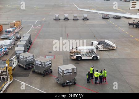 Bodenpersonal oder Gepäckabfertiger mit Bodenunterstützungsausrüstung des Flughafens warten darauf, Frachtcontainer auf ein Flugzeug/Flugzeug/Flugzeug am Flughafen Genf, Schweiz, zu laden. (128) Stockfoto