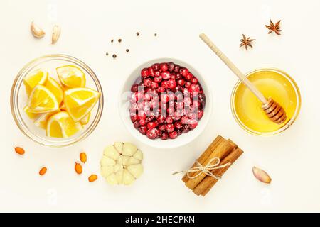 Immun stärkenden Lebensmitteln. Gesunde Lebensmittelzusammensetzung mit wilden Preiselbeeren, Honig, Knoblauch, Sanddorn, Zimtstangen und Gewürzen auf weißem Hintergrund. Stockfoto