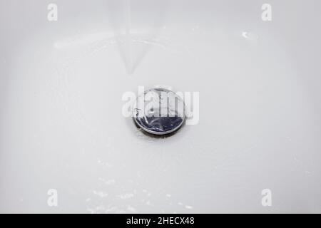 Wasser fließt im Waschbecken den Abfluss hinunter Stockfoto
