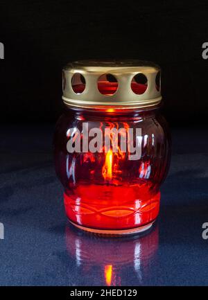 Kerze brennt in Glasform mit metallischem Deckel auf dunklem Hintergrund. Gegenstände für die Dekoration der Festtafel Stockfoto