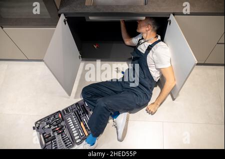 Draufsicht auf einen Mann, der auf dem Boden lag und das Waschbecken reparierte Stockfoto