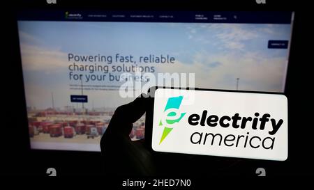 Person, die das Smartphone mit dem Logo des US-amerikanischen Elektroladerunternehmens Electrify America LLC auf dem Bildschirm vor der Website hält. Konzentrieren Sie sich auf die Telefonanzeige. Stockfoto