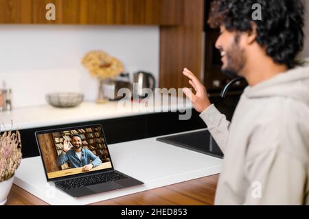 Nahaufnahme eines pakistanischen Mannes, der eine App für die Videokommunikation über Entfernungen mit Kollegen, Freunden, Online-Meetings und dem Blick und Winken auf den Laptop-Desktop mit Mitarbeiterprofilen verwendet Stockfoto