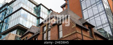 Altes Backsteingebäude mit einem modernen Bürogebäude aus Glas dahinter Stockfoto