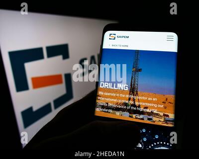 Person mit Mobiltelefon und Webseite des italienischen Oilfield-Dienstleisters Saipem S.p.A. auf dem Bildschirm mit Logo. Konzentrieren Sie sich auf die Mitte des Telefondisplays. Stockfoto