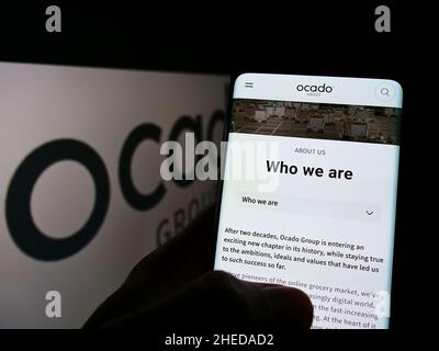 Person, die ein Smartphone mit einer Webseite des britischen Einzelhandelsunternehmens Ocado Group plc auf dem Bildschirm vor dem Logo hält. Konzentrieren Sie sich auf die Mitte des Telefondisplays. Stockfoto