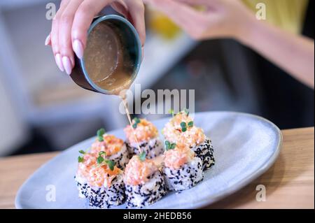 Nahaufnahme von Sushi auf dem Teller und Weiblichkeit Hände gießen Sauce Stockfoto