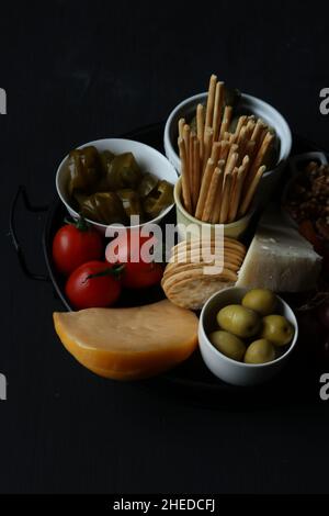 Käse, Oliven und Obst, Gemüse auf einem Teller auf schwarzem Hintergrund Stockfoto